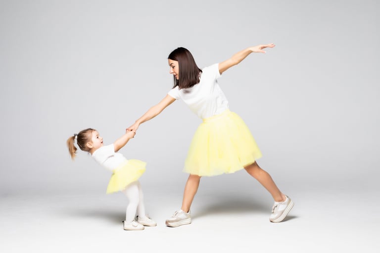 Full-length shot of cheerful adult lady and little girl in light dresses dancing on isolated background